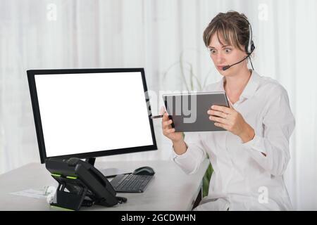 Schockierte Frau mit einem Headset im Büro, das ein digitales Tablet und einen Computerbildschirm verwendet, ist leer, um Platz für Kopien zu schaffen Stockfoto