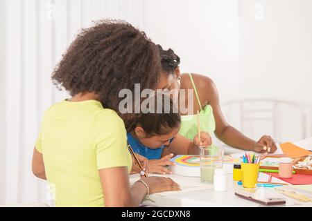 Seitenansicht eines kleinen Mädchens, das mit ihren beiden Lehrern im Kunstunterricht malt Stockfoto