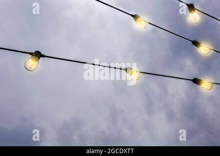 Glühende Glühbirnen hängen am dunklen Abendhimmel, in einer Reihe moderne Dekoration mit Kopierraum Stockfoto