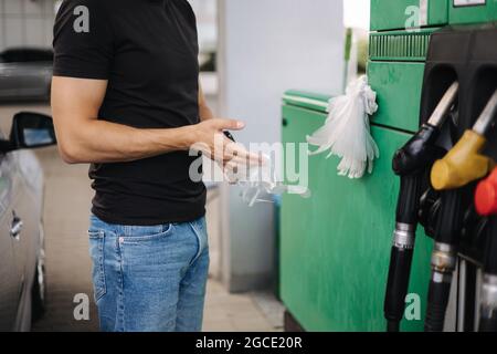 Nahaufnahme eines Mannes, der Schutzhandschuhe an der Tankstelle anlegte, um an der Tankstelle zu tanken. Konzept der Benzinpreise Stockfoto