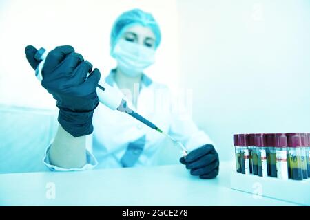 Eine Wissenschaftlerin, die im modernen chemischen Labor durch das Mikroskop schaut und dabei einige Forschungsarbeiten unternimmt. Blaue Tonung Stockfoto