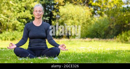 Panorama-Web-Banner-Header von reifen mittleren Alters fit gesunde Frau praktiziert Yoga außerhalb in einer natürlichen ruhigen grünen Umgebung Panorama. Stockfoto