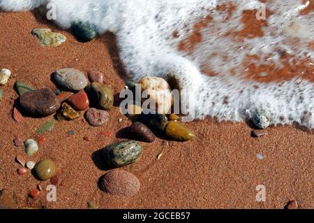 Die Wellen der Northumberland Strait waschen sich über Sand und bunte Felsen an einem Strand auf Prince Edward Island. Stockfoto