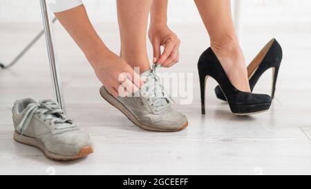 Nahaufnahme einer Geschäftsfrau, die schwarze Schuhe mit hohem Absatz auszieht und sich in bequeme Sneaker verwandelt. Stockfoto