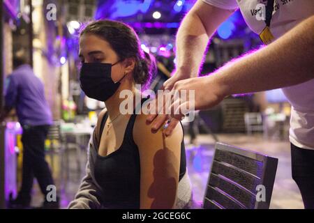 London, Großbritannien, 8. August 2021: Gabriella, 27 Jahre alt, erhält eine Dosis des Pfizer-Impfstoffs im Nachtclub Heaven, der am Sonntagnachmittag und Abend seine Türen für eine Pop-up-Impfklinik öffnete. Mitarbeiter des NHS gaben den Pfizer-Impfstoff an Erwachsene, die entweder einen ersten oder zweiten Jab wollten, um die Impfrate des Bezirks Westminster zu verbessern, die zu den niedrigsten im Land gehört. Die Tanzfläche wurde über den Impfstationen verteilt und die Stange wurde verwendet, um Dosen des Impfstoffes in Spritzen zu ziehen. Anna Watson/Alamy Live News Stockfoto