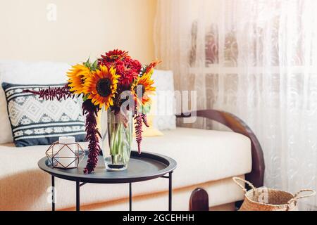 Heller Strauß von Sonnenblumen und Zinnia Blumen in Vase im Wohnzimmer gelegt. Inneneinrichtung und Inneneinrichtung. Herbst gelb rot orange Herbstblüten auf dem Tisch Stockfoto