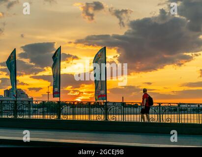 Mann, der auf der Trinity-Brücke läuft, während die Sonne aufgeht und den Himmel in gelben Farbtönen malt, 4:15 UHR morgens, St. Petersburg, Russland Stockfoto