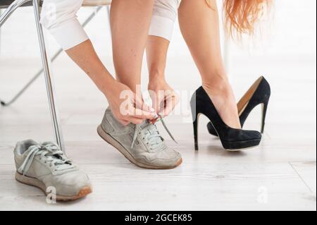 Nahaufnahme einer Geschäftsfrau, die schwarze Schuhe mit hohem Absatz auszieht und sich in bequeme Sneaker verwandelt. Stockfoto
