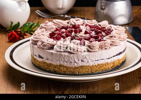 Hausgemachter Granatapfel-Käsekuchen, garniert mit Rahm und Granatapfelkernen in brauner Keramikschale mit Granatapfelblüte, weißer Kaffeetasse. Milchkrug und Stockfoto