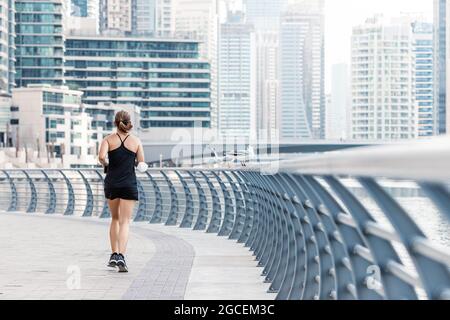 Eine nicht identifizierbare Frau macht ein Cardio-Training und läuft entlang der Uferpromenade in Dubai Marina Stockfoto