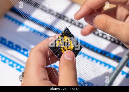 Junges Mädchen macht ein Armband mit Perlen mit ihren Händen, Ukraine, Nahaufnahme. Elemente der Stickerei aus Perlen, Gemälde und handgemachte von Meistern von Perlen Stockfoto