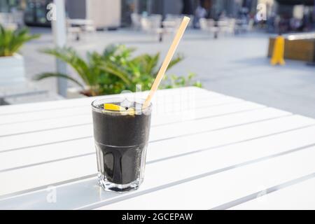 Alkoholfreies, ungewöhnliches kohlensäurehaltiges Wasser in schwarzer Farbe mit Eis und Zitrone und Trinkhalm Stockfoto