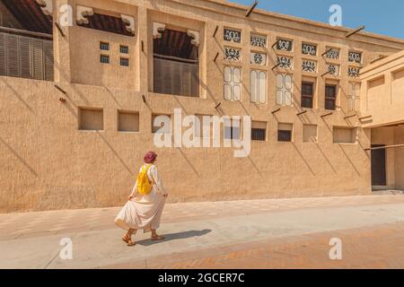 Eine Frau mit rotem Turban und einem gelben Rucksack geht durch die alten engen Straßen von Bur Dubai und Creek. Reise- und Sightseeing-Konzept Stockfoto