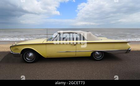 Klassisches gelbes Ford Sunliner Cabrio Auto, geparkt an der Strandpromenade Meer und Strand im Hintergrund. Stockfoto