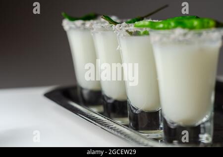 Kokosnusscocktail in einem Glas, das mit Kokosflocken und grünem Vogelauge-Chili dekoriert ist und auf einem silbernen Tablett serviert wird, mit weißen Getränken Stockfoto