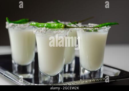 Kokosnusscocktail in einem Glas, das mit Kokosflocken und grünem Vogelauge-Chili dekoriert ist und auf einem silbernen Tablett serviert wird, mit weißen Getränken Stockfoto