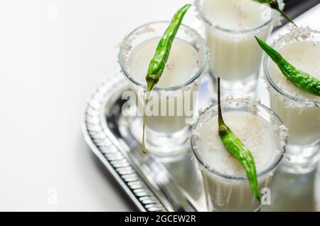 Kokosnusscocktail in einem Glas, das mit Kokosflocken und grünem Vogelauge-Chili dekoriert ist und auf einem silbernen Tablett serviert wird, mit weißen Getränken Stockfoto