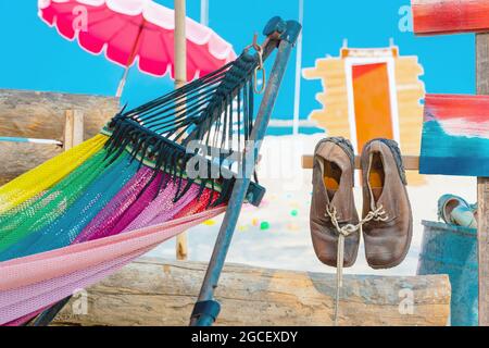 Ein Paar alte braune Lederschuhe, die mit Schnürsenkeln am alten Holzpfahl am Sandstrand zusammengebunden sind. Gebrauchte Lederstiefel Schuhe an Th Stockfoto