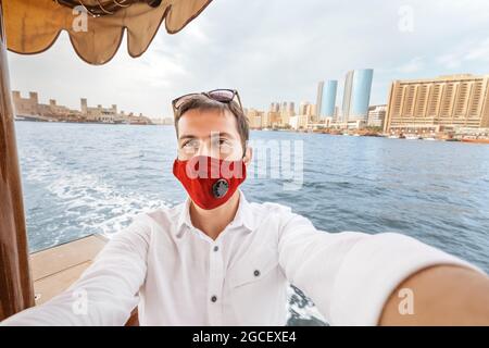 Fröhlicher Mann mit medizinischer Maske auf der traditionellen Fähre Abra Dhow auf dem Dubai Creek. Coronavirus- und Covid-19-Pandemiekonzept Stockfoto