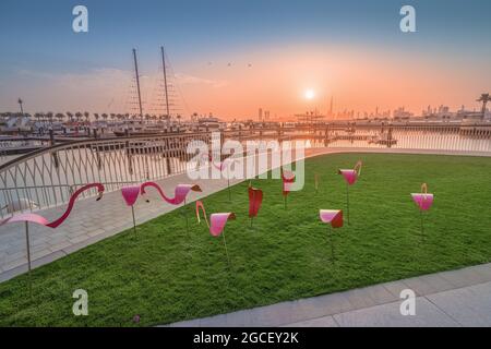 Dekorative Figuren aus rosa Flamingos auf der Promenade und weißer Bogen vor dem Hintergrund der Bucht mit Schiffen und Yachten im Yachthafen Creek Har Stockfoto