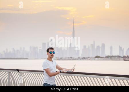 Happy man freier Programmierer und Junior-Entwickler schreibt Code und denkt vor dem Hintergrund über ein Projekt in der paradiesischen Resortstadt Dubai nach Stockfoto