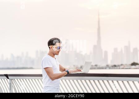 Happy man freier Programmierer und Junior-Entwickler schreibt Code und denkt vor dem Hintergrund über ein Projekt in der paradiesischen Resortstadt Dubai nach Stockfoto