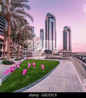 Dekorative Figuren von rosa Flamingos auf der Promenade vor dem Hintergrund der Bucht mit Schiffen und Yachten im Hafen von Marina Creek in Dubai Stockfoto