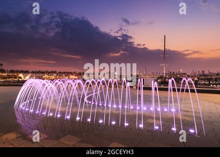 Parken von Yachten und Schiffen im Hafen von Dubai Creek Marina mit Blick auf das Stadtzentrum und einem beleuchteten Brunnen Stockfoto