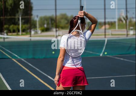 Frau im Rock steht zurück auf dem Tennisplatz und hält den Schläger. Stockfoto