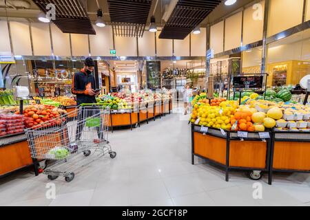 23. Februar 2021, Dubai, VAE: Der Kurier für die Lebensmittelzustellung wählt in einer medizinischen Maske Gemüse und Obst in einem Supermarkt aus Stockfoto
