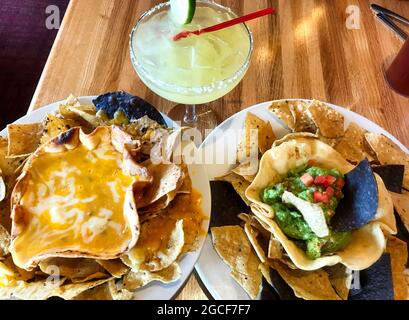 Eine gekühlte Margarita und köstliche Vorspeisen mit Käse und Guacamole Dips, serviert in Taco Shell Bowls, mit blauen und gelben Maischips. Stockfoto