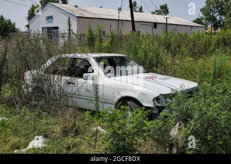 Verlassene zerstörte Auto links entlang der Straße in Pinsel und Unkraut. Stockfoto