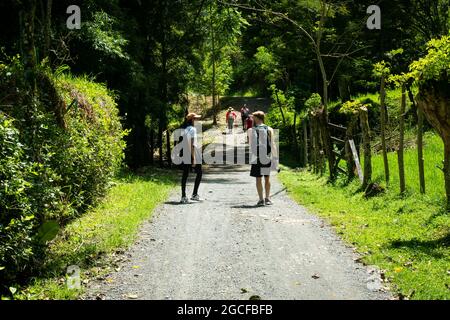 Amada, Antioquia, Kolumbien - Juli 18 2021: Kaukasischer blonder Mann mit einer Lateinerin, der an einem sonnigen Tag auf einer schmutzigen Straße unterwegs ist Stockfoto