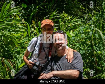 Amaga, Antioquia, Kolumbien - Juli 18 2021: Lateinische Frau mit orangefarbener Kappe umarmt einen kaukasischen Mann in der Natur Stockfoto