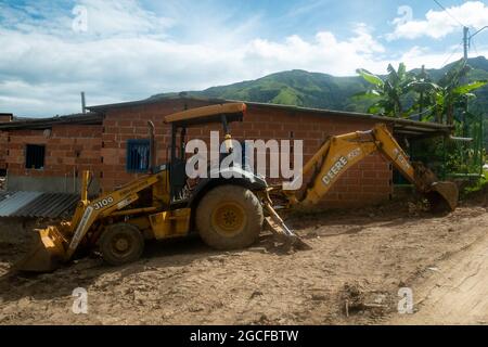 Amaga, Antioquia, Kolumbien - Juli 18 2021: Gelber Kranich entfernt einen Erdhaufen neben einem Ziegelhaus Stockfoto