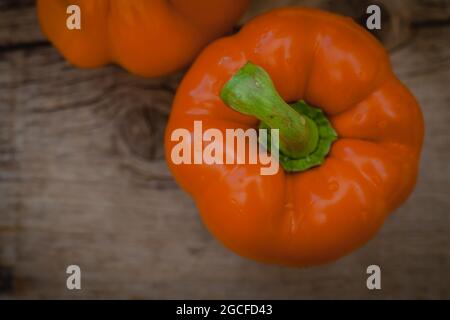Orangefarbene Paprika mit glänzenden Wassertropfen auf rustikalem Holzhintergrund Stockfoto