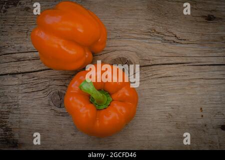 Orangefarbene Paprika mit glänzenden Wassertropfen auf rustikalem Holzhintergrund Stockfoto