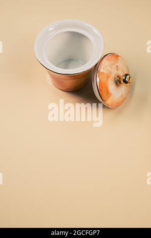 Eine Nahaufnahme einer orangefarbenen leeren Tasse neben einer Abdeckung auf einem orangefarbenen isolierten Hintergrund mit freiem Platz Stockfoto