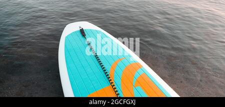 Nahaufnahme des Stand Up SUP Paddle Boards auf See oder Meer mit blauen Seerosen, paddeln im Sommer bei Sonnenuntergang. Sommerurlaub mit der Familie Stockfoto