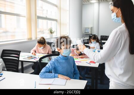 Rückkehr Zur Schule. Lehrer mit digitalen medizinischen kontaktlosen Infrarot-Thermometer, Messung und Kontrolle der Körpertemperatur, Screening klein Stockfoto