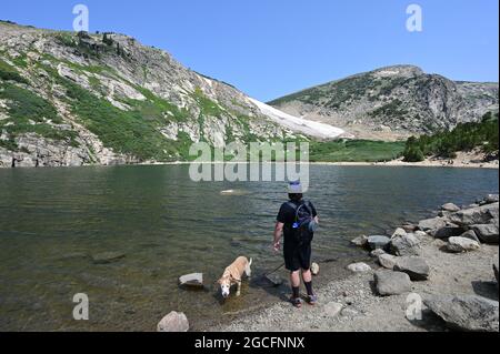 Mann und Hund am Saint Mary's Lake unter dem St. Mary's Glacier im Arapaho National Forest, Colorado, an einem sonnigen Sommermorgen. Stockfoto