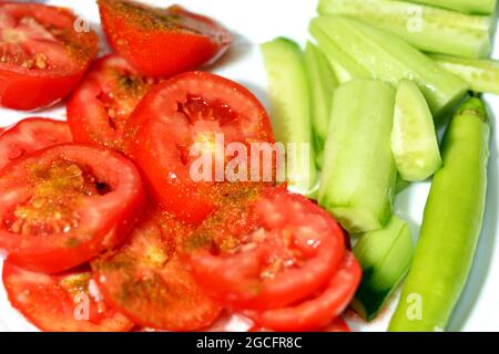 Scheiben gesalzener Tomaten mit Kreuzkümmel, Gurke und scharfem grünen Pfeffer auf einem weißen Teller, gesundes Lebensmittelkonzept, frisch geschnittene Tomaten und Gurken Stockfoto