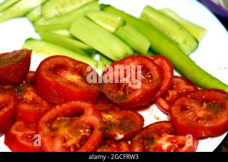 Scheiben gesalzener Tomaten mit Kreuzkümmel, Gurke und scharfem grünen Pfeffer auf einem weißen Teller, gesundes Lebensmittelkonzept, frisch geschnittene Tomaten und Gurken Stockfoto