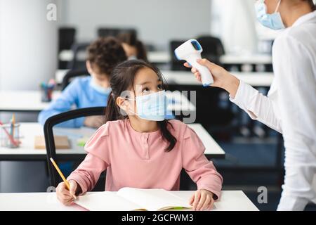 Zurück Zur Schule Konzept. Lehrer oder Krankenschwester mit berührungsloser elektronischer Infrarot-Laserpistole, Messung und Körpertemperatur auf der Stirn, Überprüfung littl Stockfoto