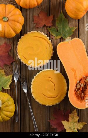 Traditionelles Thanksgiving Dessert Offene Kürbiskuchen mit zwei Gabeln, leuchtend orangefarbenen Kürbissen und marmorblättern auf Vintage-Holzhintergrund oben serviert Stockfoto