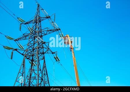 Hochspannungs-Hochspannungsleitung, Turmarbeiter mit Kran und blauem Himmel. Hydro-Linemen an Auslegerliften, die an Hochspannungstürmen arbeiten. Stockfoto