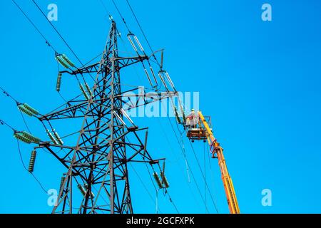 Hochspannungs-Hochspannungsleitung, Turmarbeiter mit Kran und blauem Himmel. Hydro-Linemen an Auslegerliften, die an Hochspannungstürmen arbeiten. Stockfoto