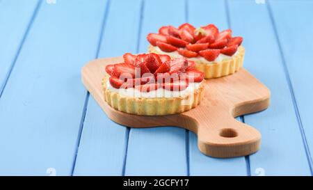 Tartlets mit frischen, saftigen Erdbeeren und Mascarpone auf Holzschnitt Brett auf hellblauem Hintergrund Copyspace Stockfoto