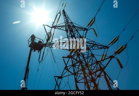 Hochspannungs-Hochspannungsleitung, Turmarbeiter mit Kran und blauem Himmel. Hydro-Linemen an Auslegerliften, die an Hochspannungstürmen arbeiten. Stockfoto