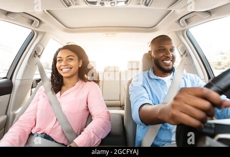 Vorderansicht Porträt eines lächelnden, hübschen afroamerikanischen Mannes, der mit einem modernen Luxusauto fährt, einer glücklichen, schönen jungen Frau, die auf dem Beifahrermeer sitzt Stockfoto